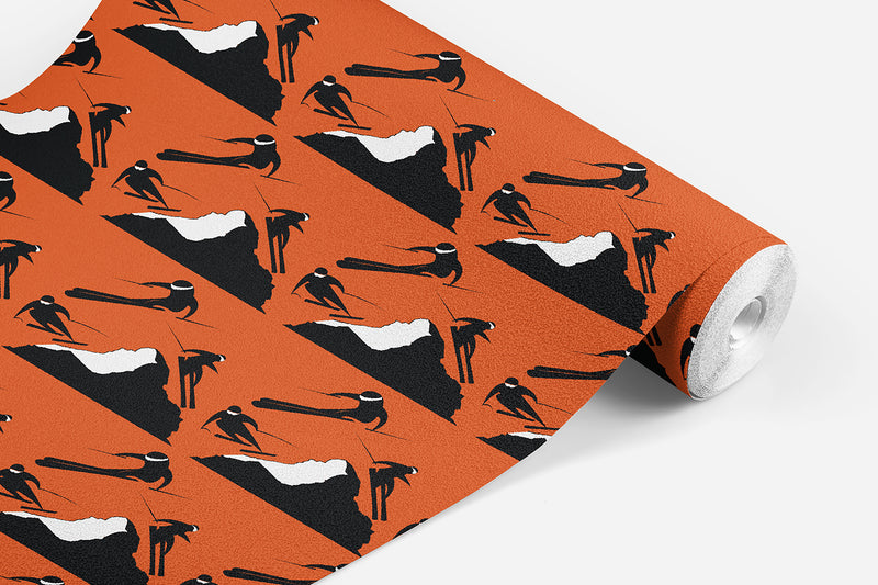 roll of Off Piste wallpaper which has black and white skiers on either side of a mountain on a orange background